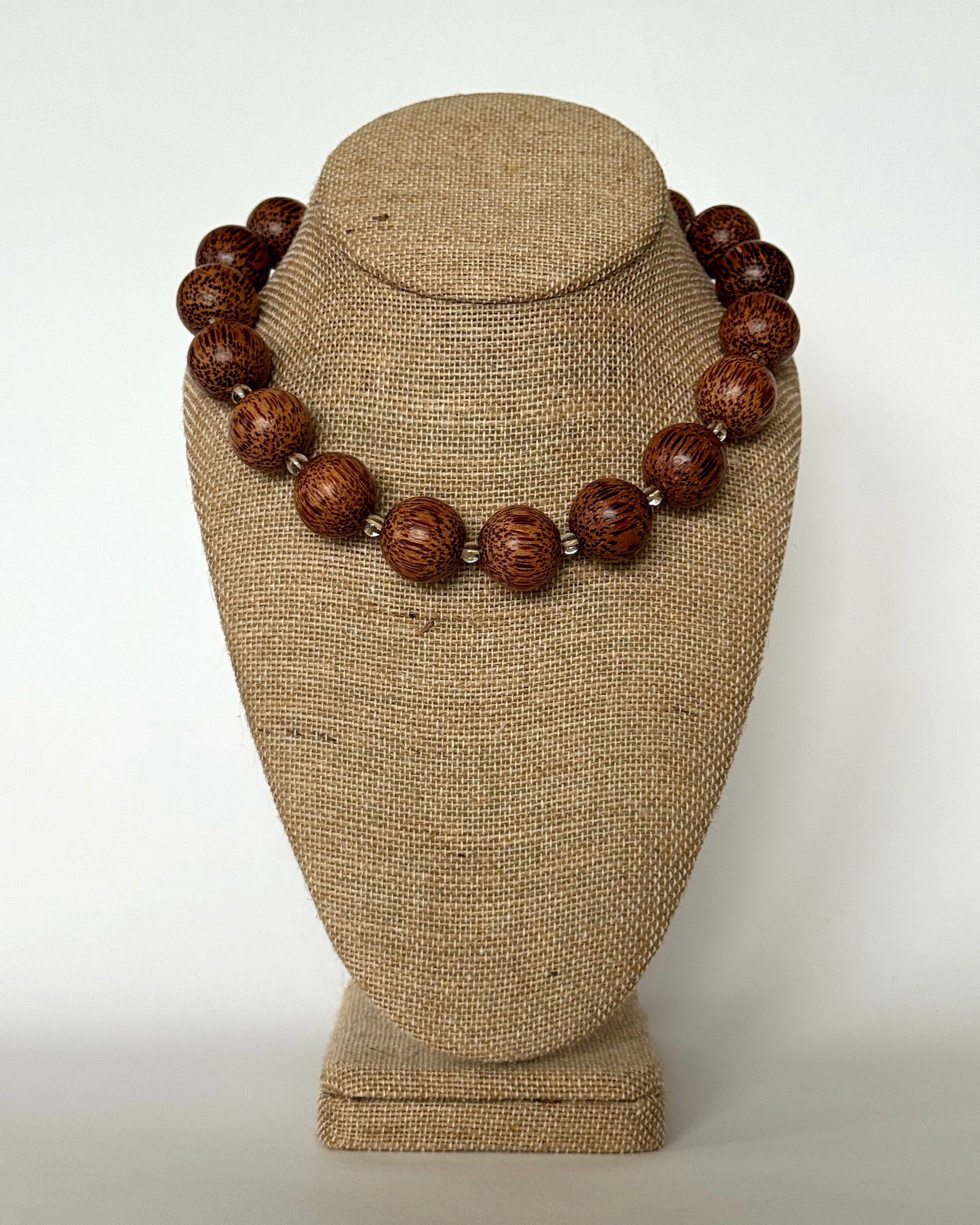 Wooden beaded necklace on a textured beige stand against a white background